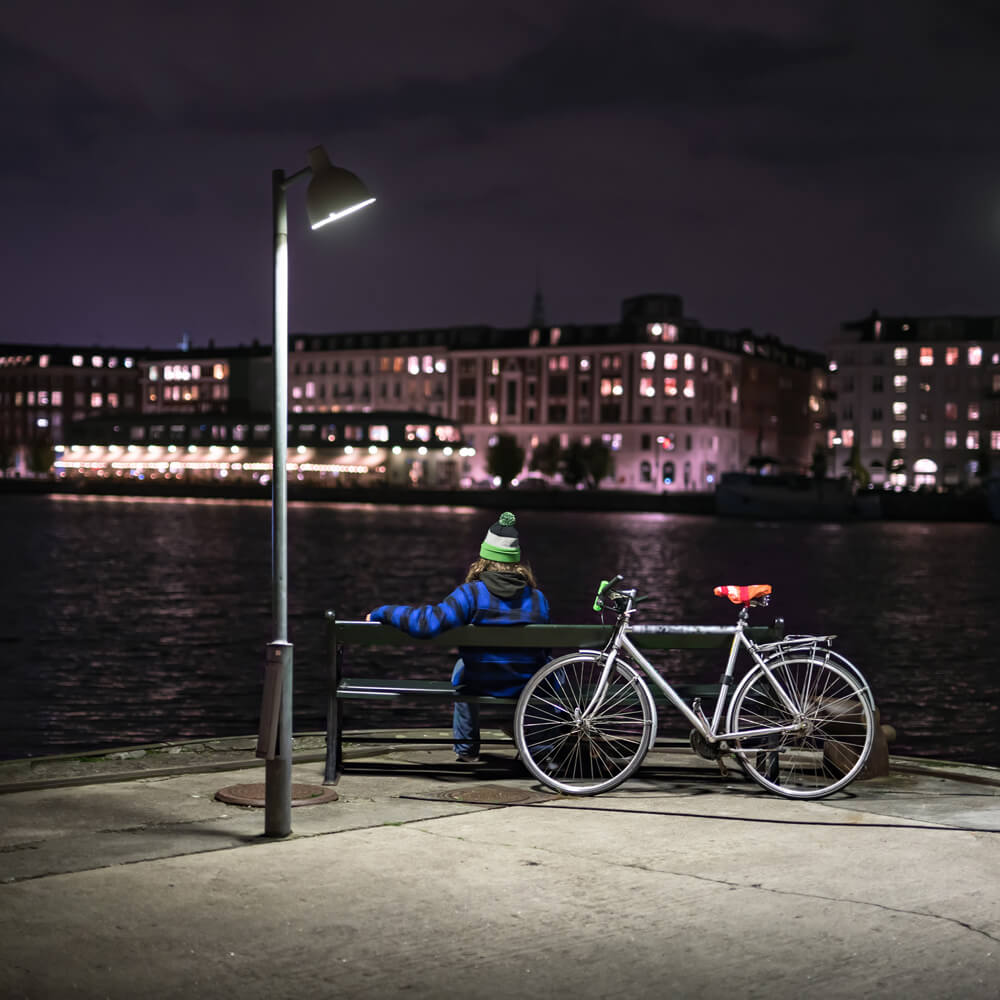 Kvinde sidder på oplyst bænk og kigger på byen