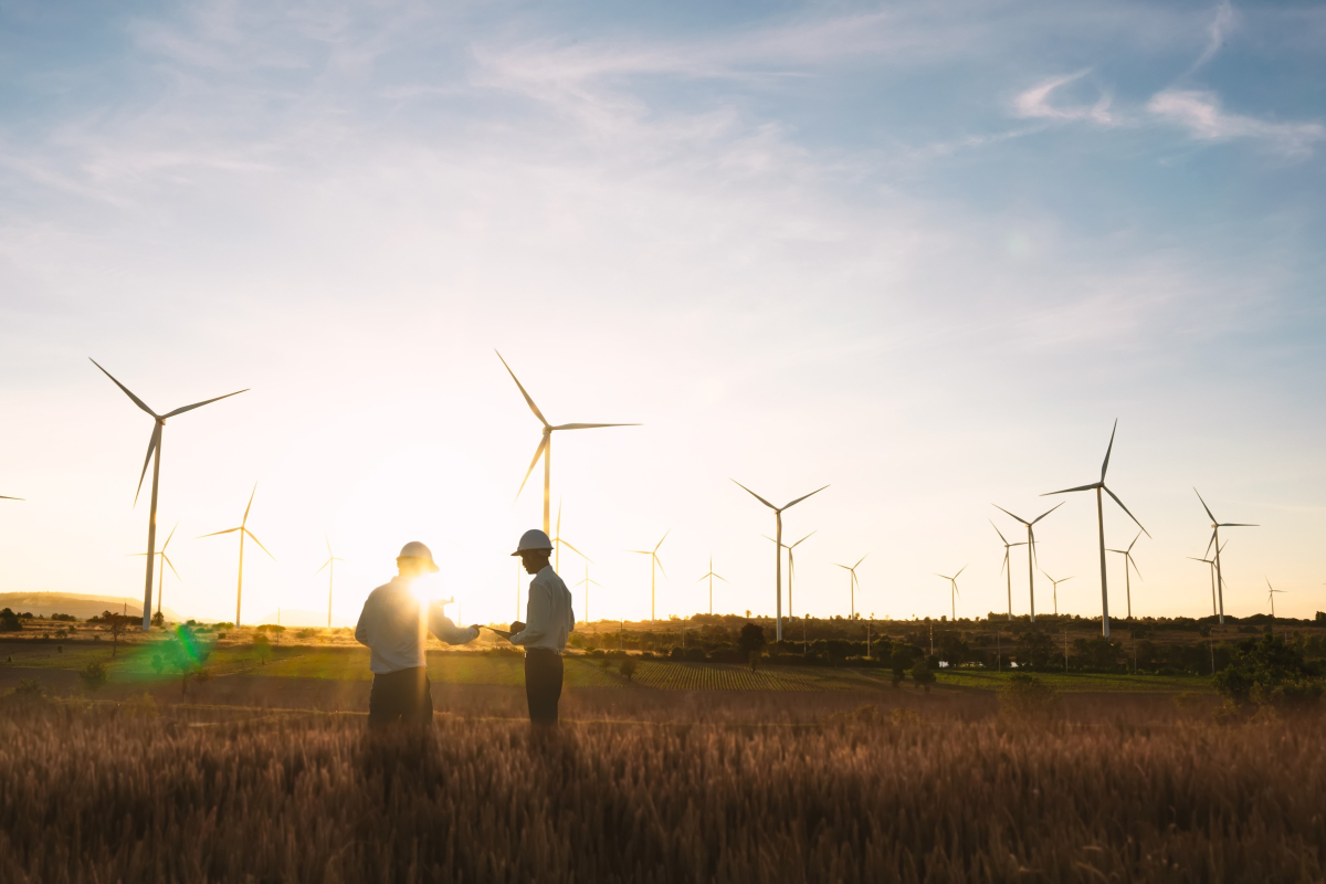 To arbejdere der står på en mark med vindmøller i baggrunden
