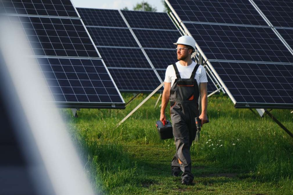 En mand med arbejdstøj og hjelm på går mellem solceller på land